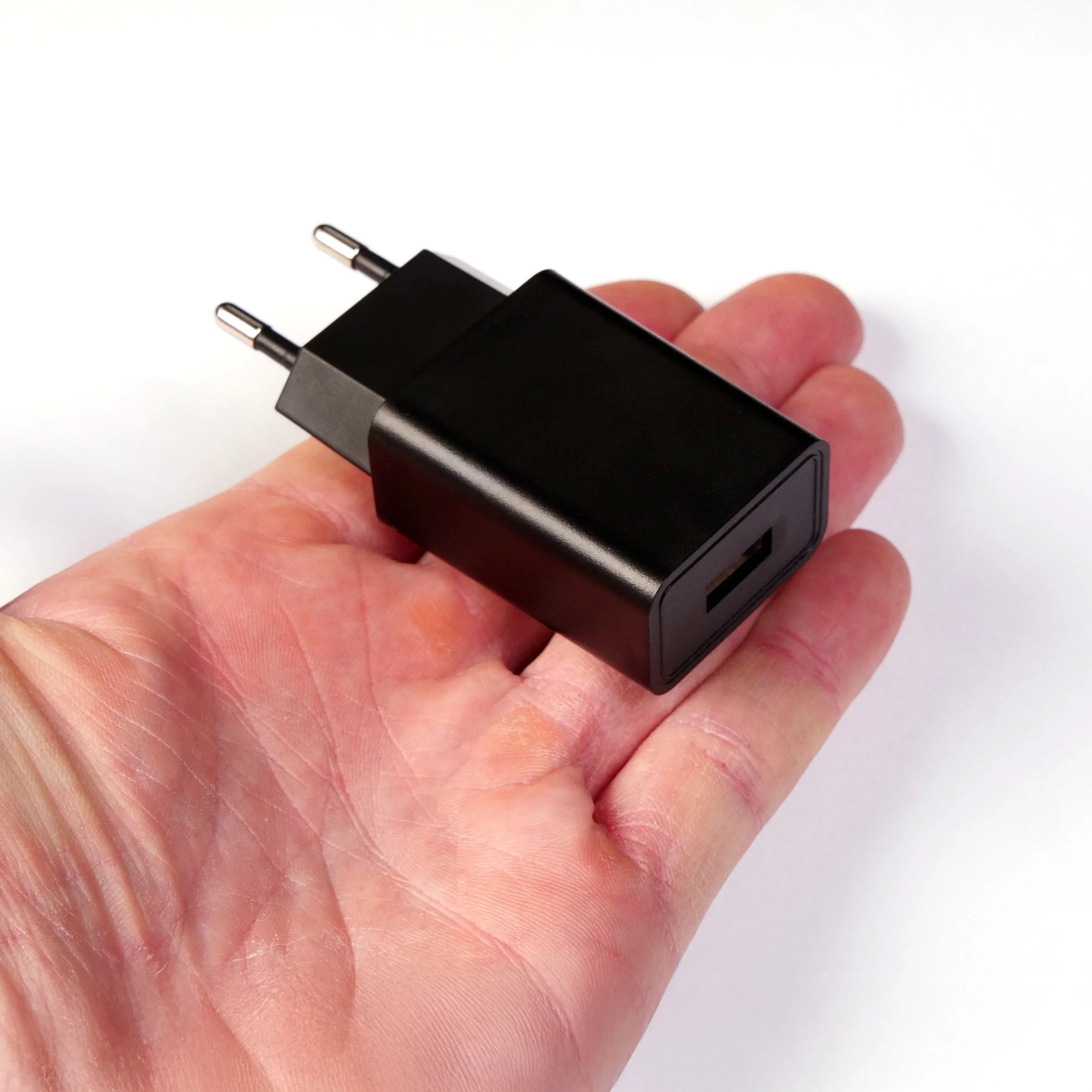 Chargeur USB noir compact posé sur une main, accessoire électronique pratique