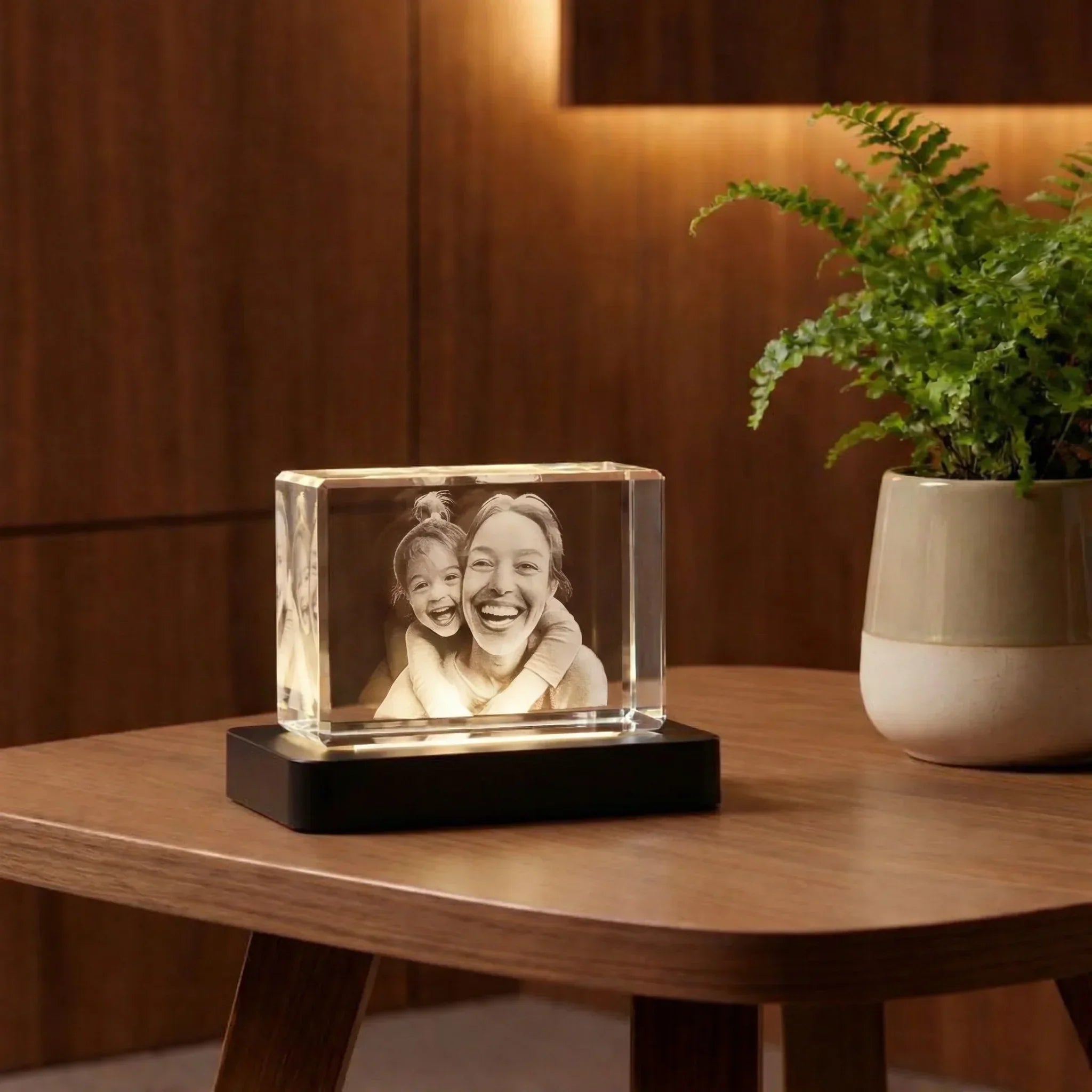 Photo gravée 3D dans un bloc de verre posée sur une table en bois, plante décorative