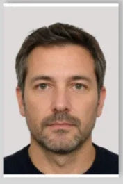 Portrait d'un homme barbu avec un regard sérieux sur fond gris clair.